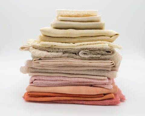 Stapel gefalteter Stoffe in verschiedenen natürlichen Beige-, Rosa- und Orangetönen.