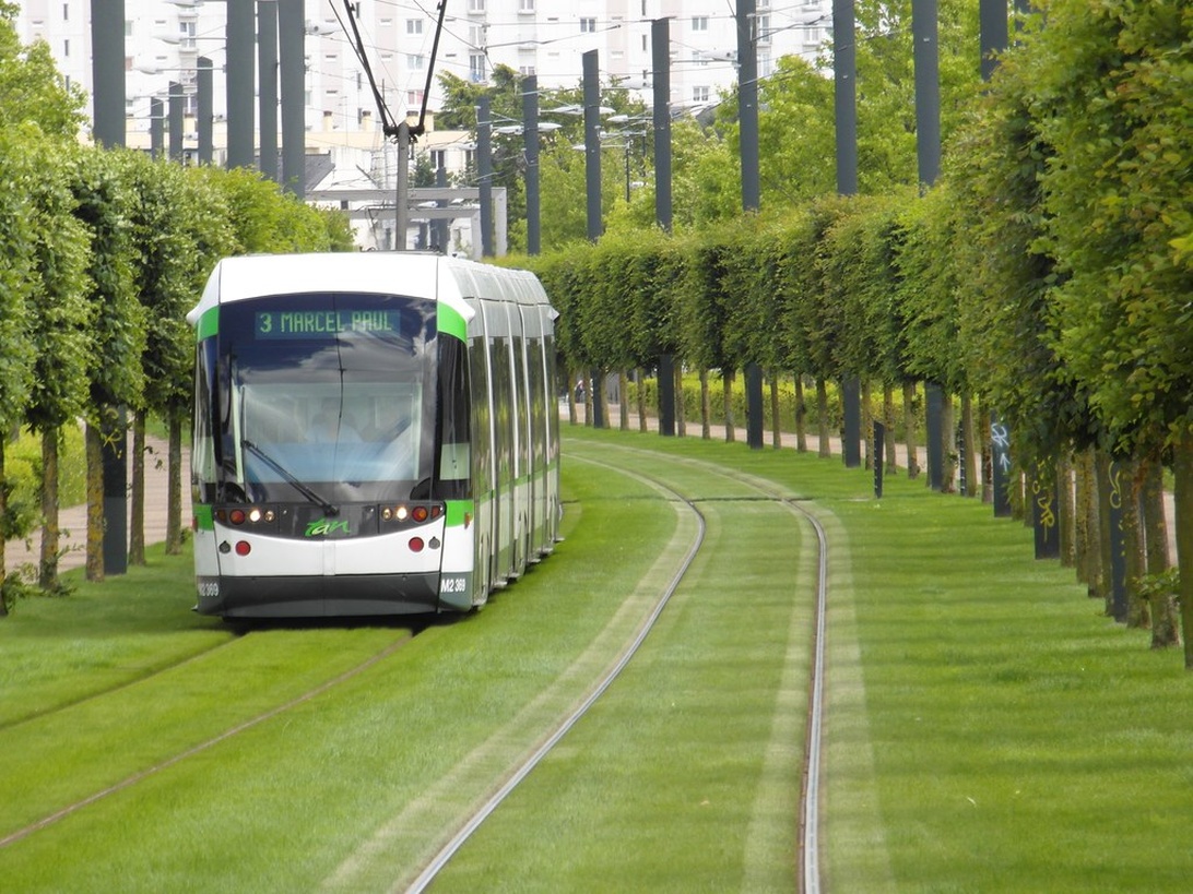 Moderne elektrische Straßenbahn auf grasbewachsenen Gleisen als Beispiel für nachhaltige Stadtlogistik.
